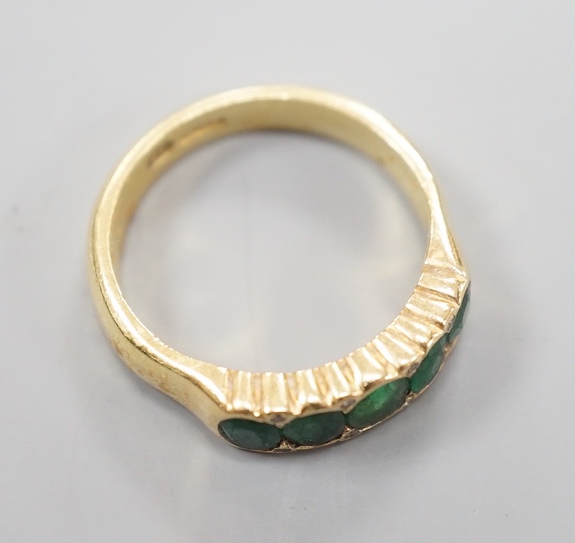 A modern 18ct gold and graduated five stone emerald set half hoop ring, with diamond chip spacers, size Q/R, gross weight 7.5 grams.